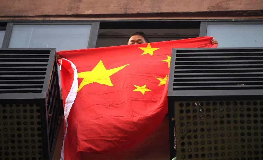 A resident unfurls the Chinese national flag from his building window in front of the US consulate in Chengdu, 26 July 2020. (Noel Celis/AFP)