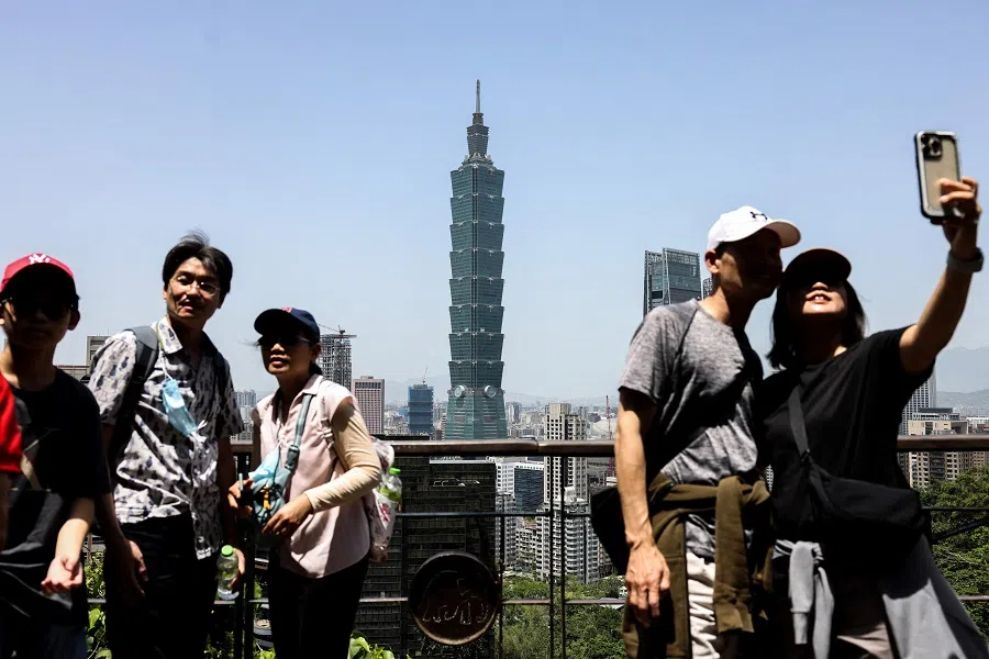 People pose for photographs as the landmark Taipei 101 building is seen in the background in Taipei on 14 April 2025. (I-Hwa Cheng/AFP)
