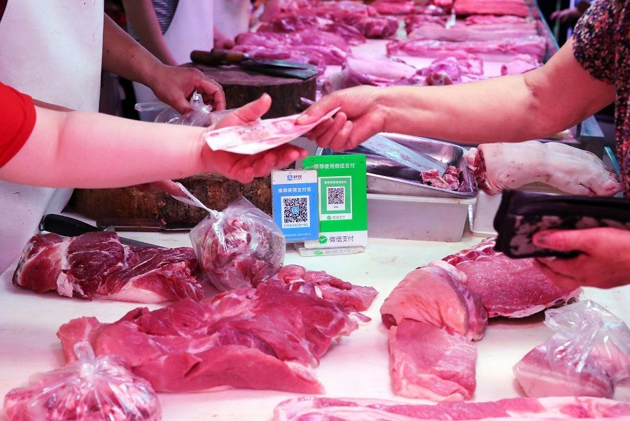 Alipay and wechat QR codes for online payment are displayed as a vendor (left) receives money from a customer at a meat stall in Nantong, Jiangsu, China, on 9 August 2018. (AFP)