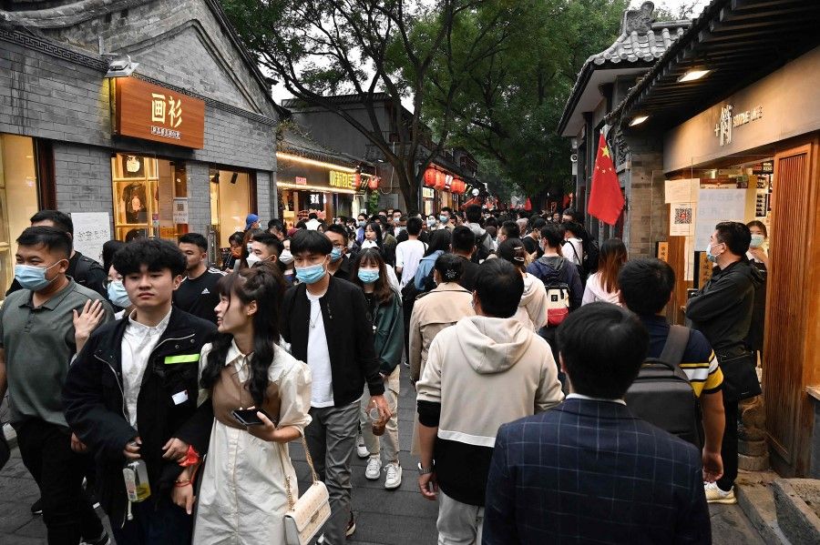 People walk in a commercial street named Nanluoguxiang during the country's national "Golden Week" holiday in Beijing on 2 October 2021. (Jade Gao/AFP)