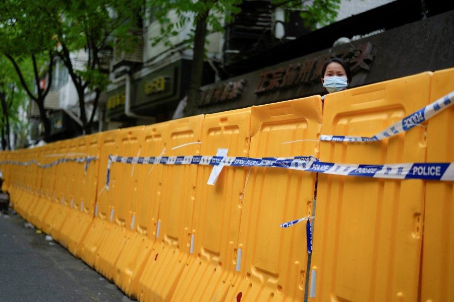 A woman looks over a barrier at an area under lockdown amid the Covid-19 pandemic, in Shanghai, China, 13 April 2022. (Aly Song/Reuters)