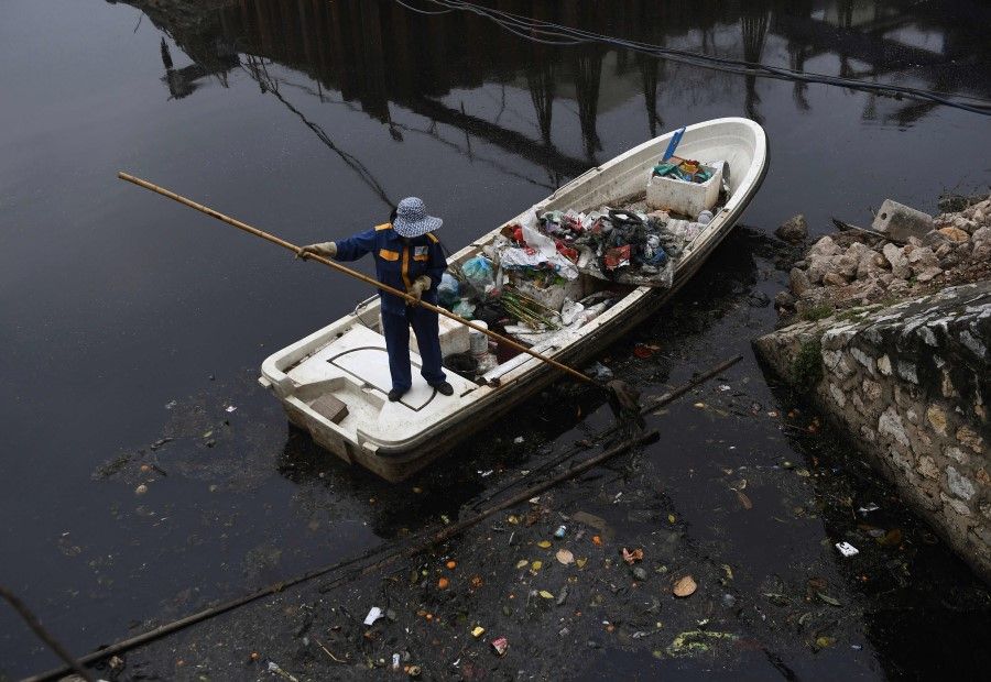 A worker collects rubbish on a drainage canal in Hanoi on 26 February 2021. (Nhac Nguyen/AFP)
