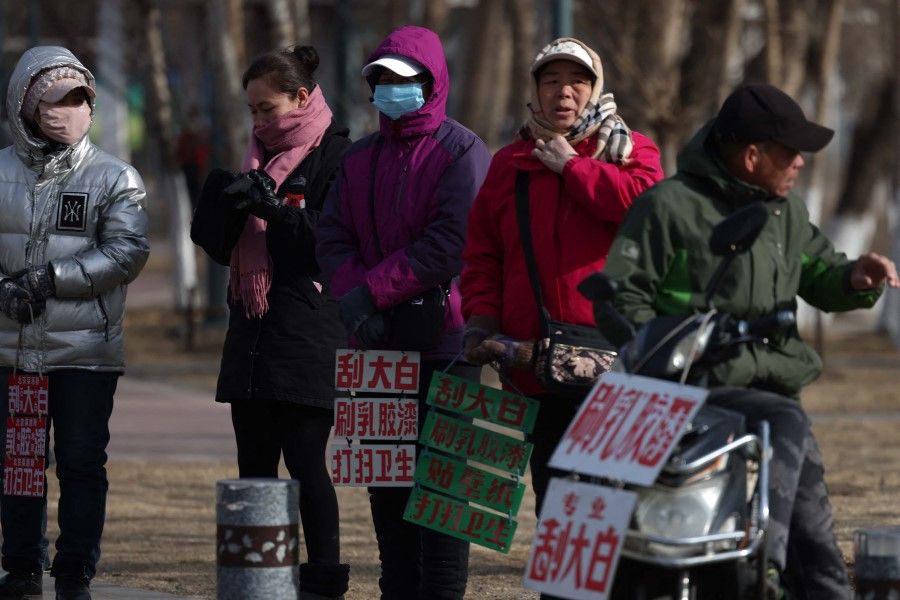 This photo taken on 1 March 2023 shows workers standing near signs advertising their skills as they wait on the street to be hired in Shenyang, in northeastern China's Liaoning province. (AFP)
