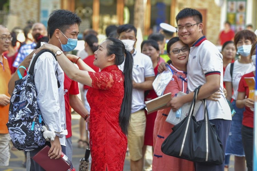 Two mothers in red qipaos hug their children at an exam centre in Hainan, 7 July 2020. (Luo Yunfei/CNS)