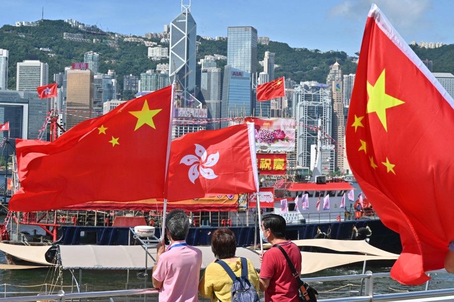 People wave Chinese and Hong Kong flags as fishing boats with banners and flags to mark the 25th anniversary of the Handover of Hong Kong from Britain to China sail through Hong Kong's Victoria harbour on 28 June 2022. (Peter Parks/AFP)