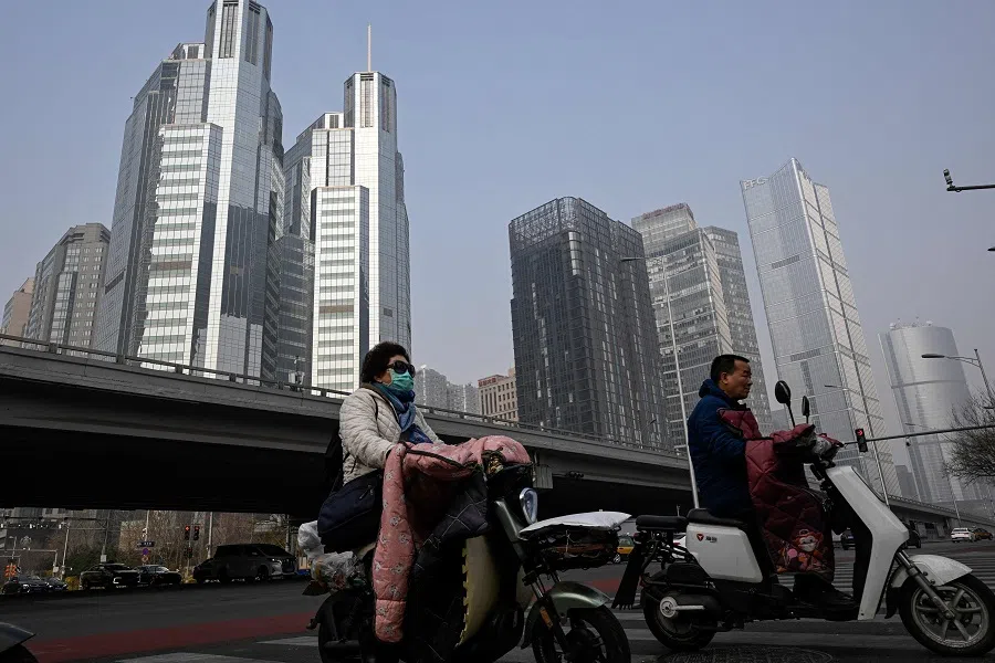 People ride scooters along a street at the central business district in Beijing, China, on 5 March 2023 (Jade Gao/AFP)