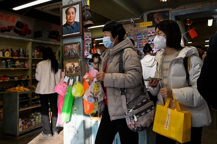 People shop at a store with a picture of late communist leader Mao Zedong hanging on the wall at the Nanluoguxiang alley in Beijing, China, on 3 March 2023. (Jade Gao/AFP)