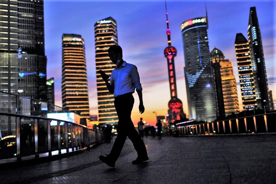 A man checks his phone while walking in Lujiazui financial district during sunset in Pudong, Shanghai, China, 13 July 2021. (Aly Song/Reuters)