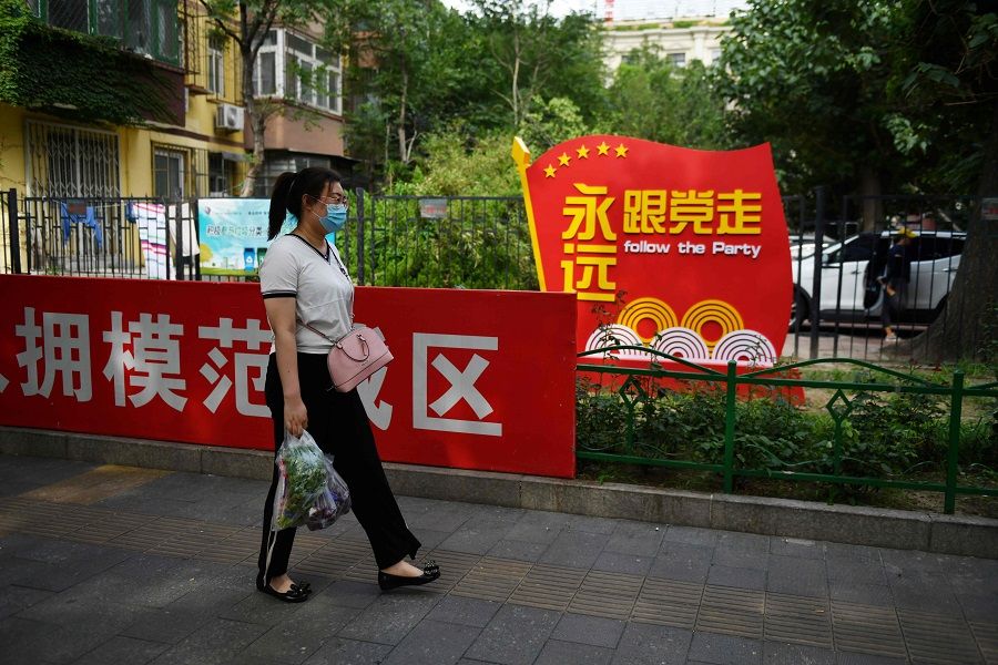 A woman walks past a Communist Party slogan urging people to "Follow the Party forever" outside a residential compound in Beijing on 6 July 2020. (Greg Baker/AFP)