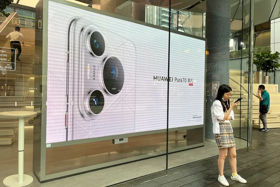 A woman uses her cellphone while standing in front of a screen advertising Huawei Pura 70 series smartphones outside Huawei’s flagship store in Shenzhen, China, on 26 April 2024. (David Kirton/Reuters)