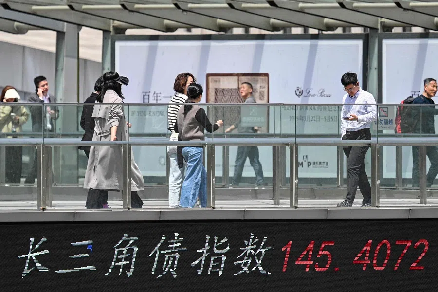 People walk across a bridge with a stocks indicator board at the financial district in Shanghai, China, on 7 April 2025. (Hector Retamal/AFP)