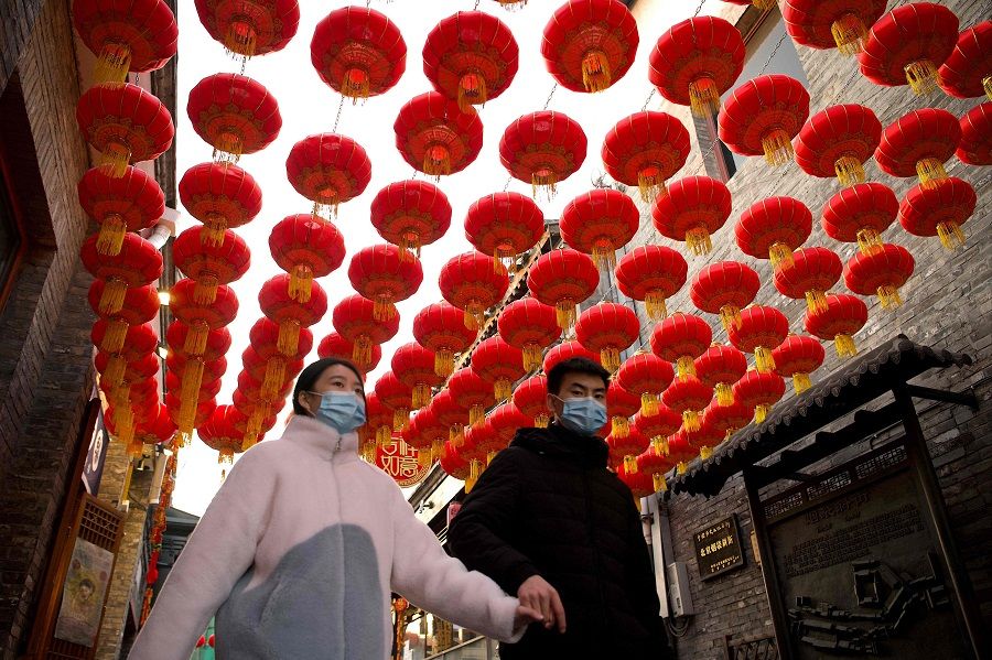 People walk under traditional Chinese lanterns along an alley in Beijing on 9 February 2021, ahead the biggest holiday of the year, the Lunar New Year, which ushers in the Year of the Ox on 12 February. (Noel Celis/AFP)