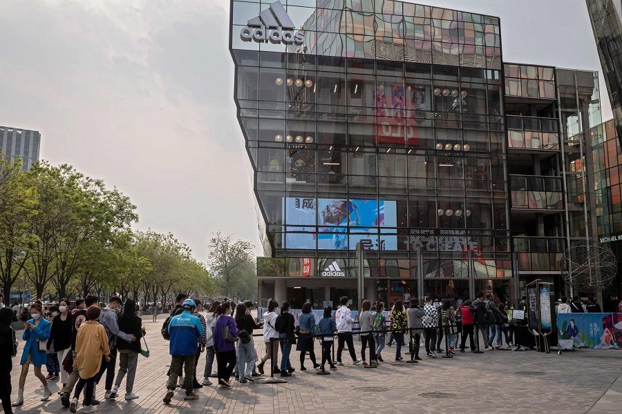 People wearing face masks amid concerns over the Covid-19 coronavirus queue to get their temperature checked before entering a shopping mall in front of an Adidas retail store (back) in Beijing on 19 April 2020. (Nicolas Asfouri/AFP)