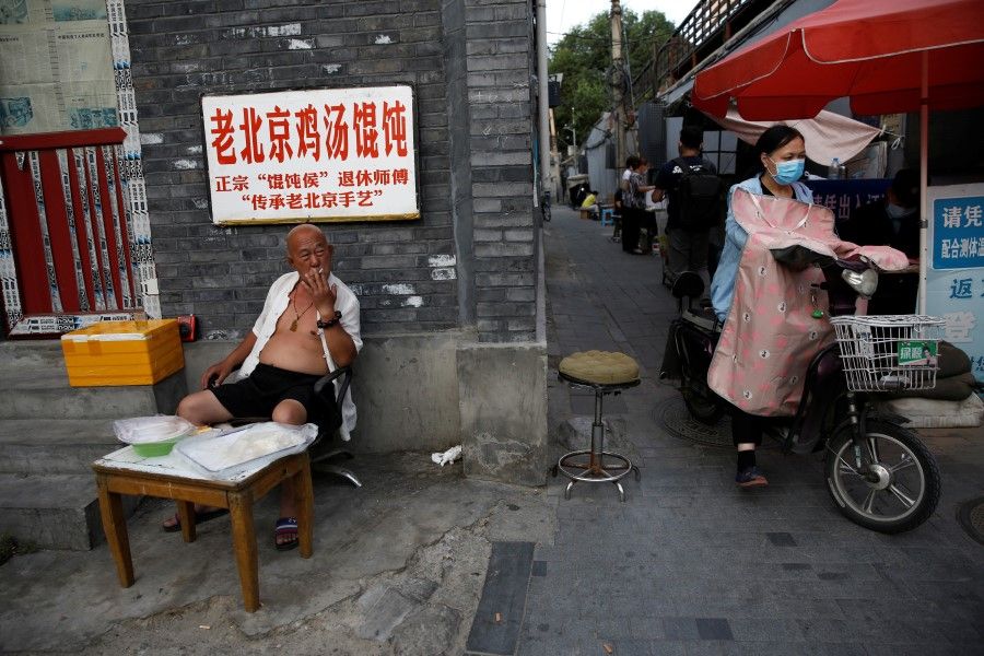 A man smokes at a stall selling frozen wonton near a hutong neighborhood in Beijing, 5 June 2020. (Tingshu Wang/REUTERS)
