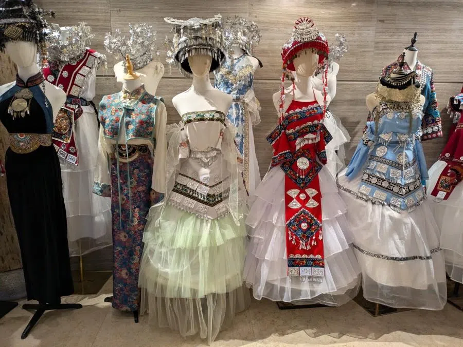 A wide selection of Miao ethnic costumes available in a travel photography shop.