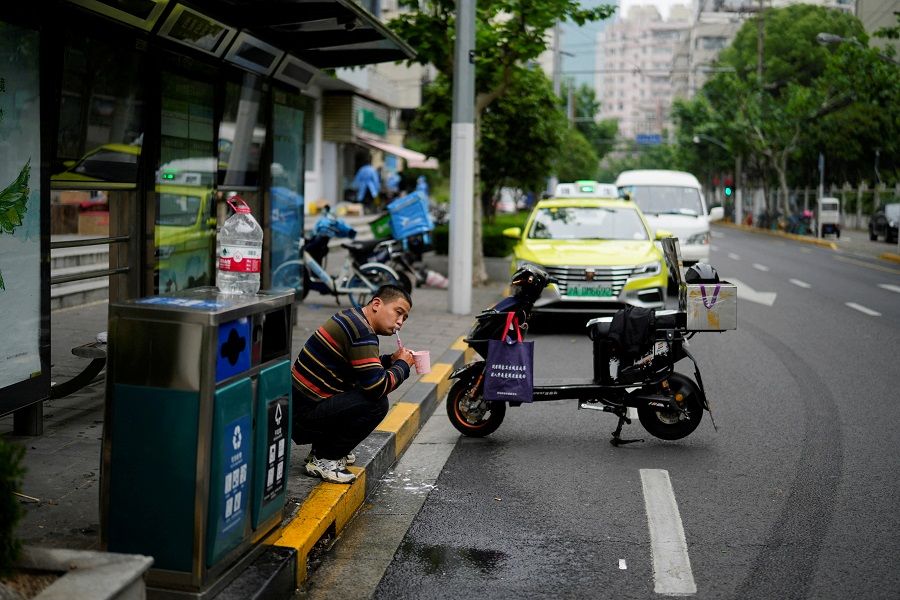 A delivery worker, who says he is living at a bus stop because he has been unable to return home for weeks due to the lockdown, brushes his teeth on a street, amid the Covid-19 pandemic, in Shanghai, China, 12 May 2022. (Aly Song/Reuters)