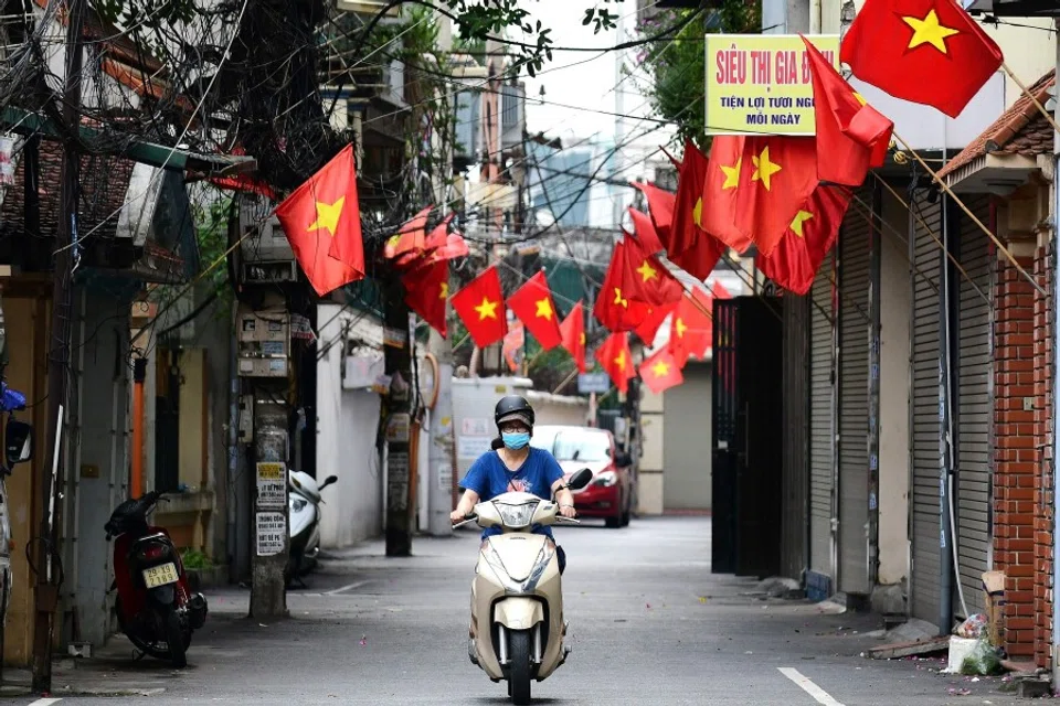 A woman rides a scooter along a street decorated with Vietnamese national flags ahead of Vietnam's National Day celebrations in Hanoi on 1 September 2021. (Nhac Nguyen/AFP)