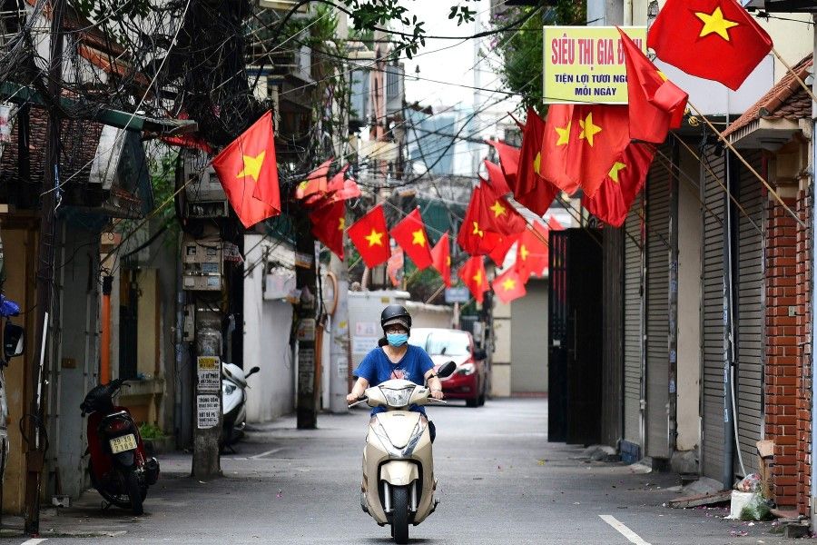 A woman rides a scooter along a street decorated with Vietnamese national flags ahead of Vietnam's National Day celebrations in Hanoi on 1 September 2021. (Nhac Nguyen/AFP)