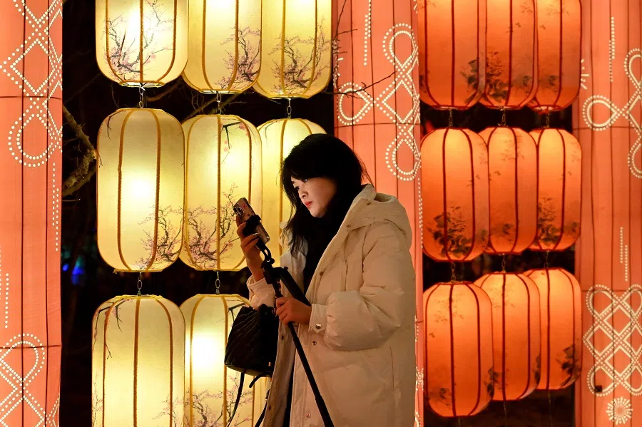 A woman looks at her phone in front of lanterns at Beijing’s Wenyuhe Park on 4 January 2025. (Adek Berry/AFP)