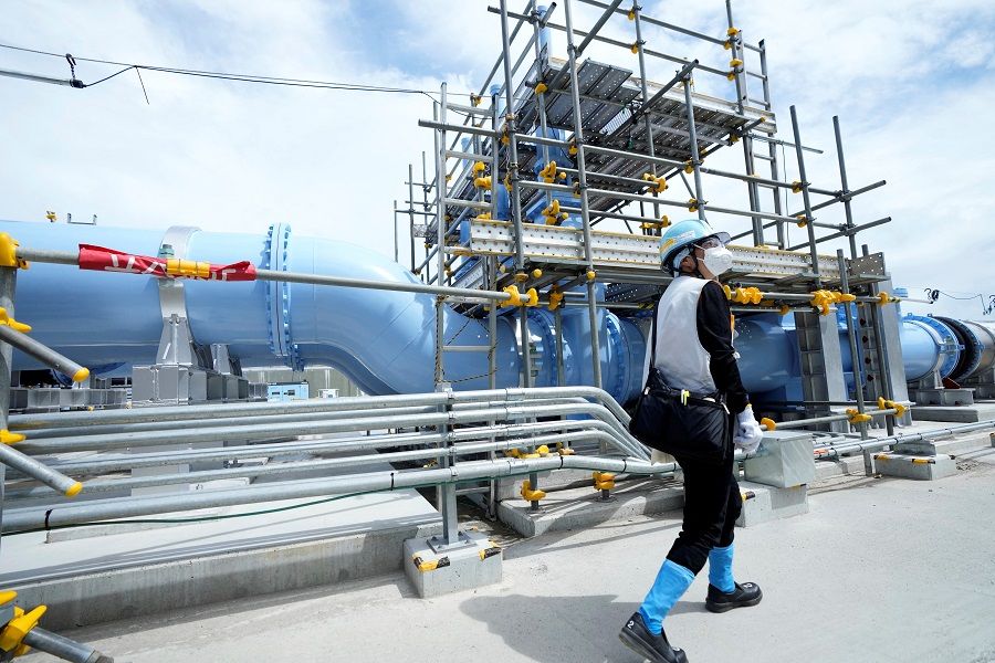 A person walks past a blue pipeline to transport seawater, part of the facility for releasing treated radioactive water to sea from the Fukushima Daiichi nuclear power plant, operated by Tokyo Electric Power Company Holdings, also known as TEPCO, during a treated water dilution and discharge facility tour for foreign media, in Futaba town, Fukushima, Japan, on 27 August 2023. (Eugene Hoshiko/Pool via Reuters)