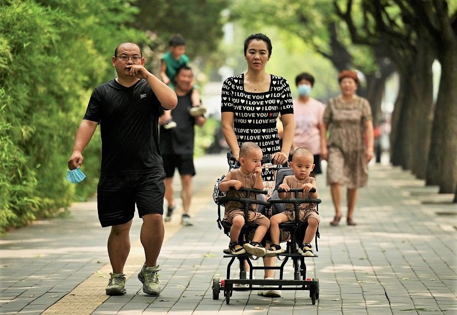 This file photo taken on 2 August 2022 shows a woman pushing a trolley with twins along a street in Beijing, China. (Noel Celis/AFP)