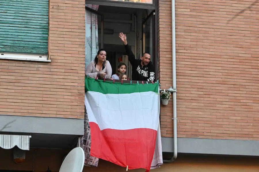 People sing, wave and clap their hands next to an Italian flag, during a flash mob "Una canzone per l'Italia" (A song for Italy) at the Magliana district in Rome on March 15, 2020. (Andreas Solaro/AFP)