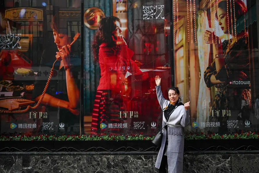 The photo taken on 7 January 2024 shows a woman posing next to the posters of Chinese television series Blossoms Shanghai directed by Hong Kong director Wong Kar-wai, in Shanghai, China. (AFP)