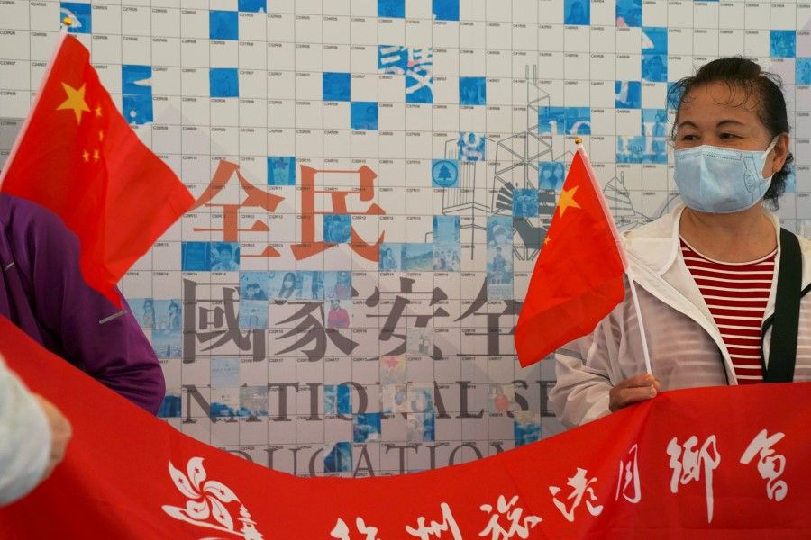 Pro-government supporters holding Chinese flags pose for pictures in front of a community mosaic wall promoting the National Security Education Day in Hong Kong, China, 15 April 2021. (Lam Yik/Reuters)