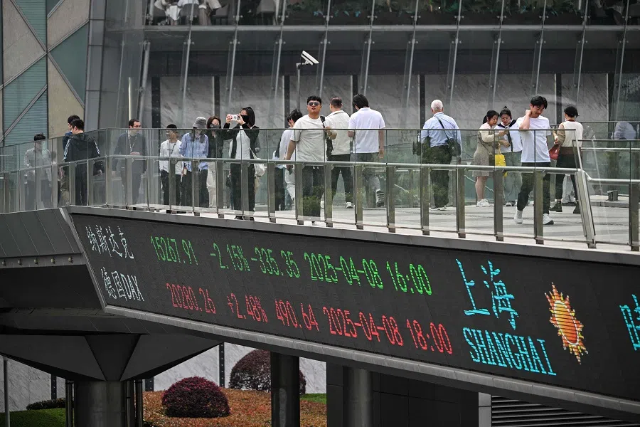 People walk across a foot bridge showing a screen displaying financial markets information at the financial district in Shanghai, China, on 9 April 2025. (Hector Retamal/AFP)