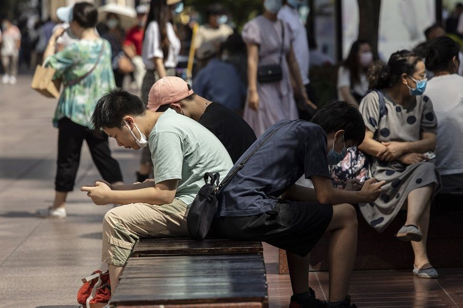 Teenagers play games on their phone while sitting on a bench at Nanjing Road East in Shanghai, China, on 3 October 2021. (Qilai Shen/Bloomberg)