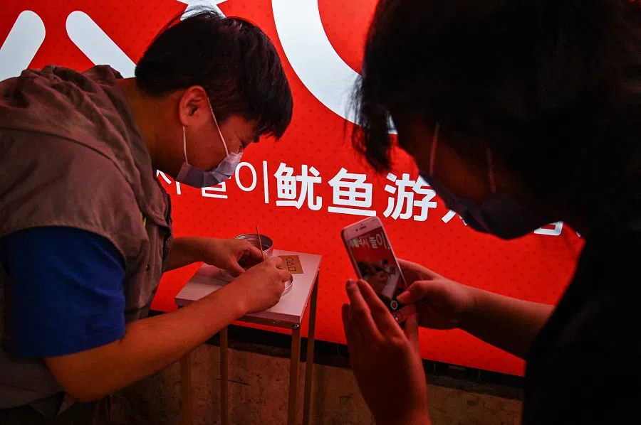 This photo taken on 12 October 2021 shows a customer cutting a dalgona, a crisp sugar candy featured in the Netflix series Squid Game, in Shanghai, China. (Hector Retamal/AFP)