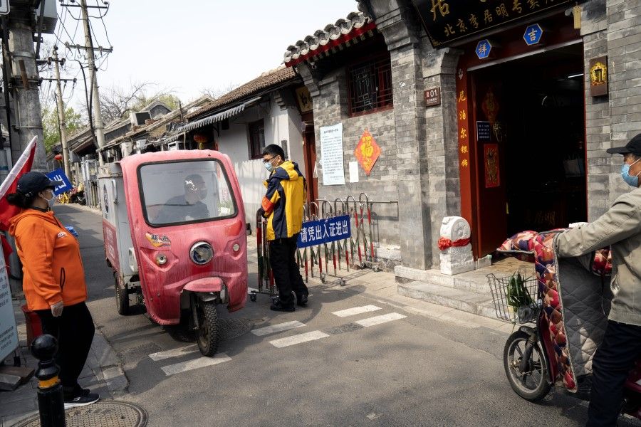 An auto rickshaw driver speaks to a pedestrian in an alleyway in Beijing, April 7, 2020. The sign on the gate says that passes are required to move in and out. (Giulia Marchi/Bloomberg)