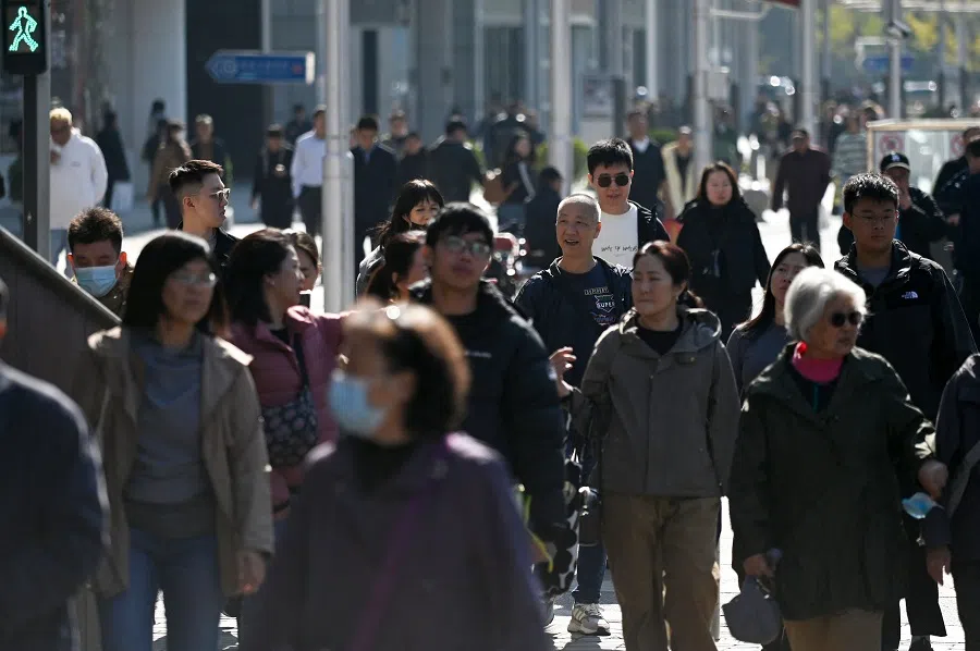 People cross a street at a business district in Beijing on 23 October 2024. (Wang Zhao/AFP)