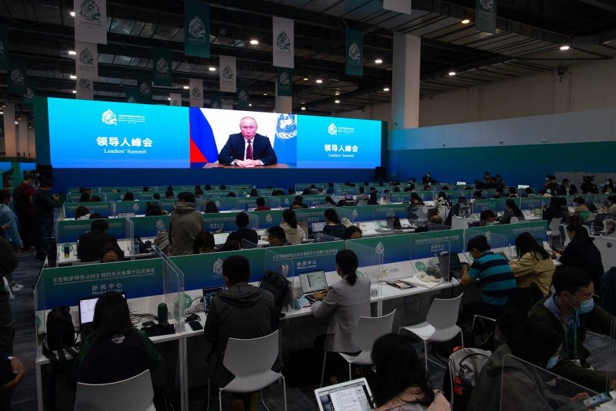 Media staff members watch a live image of Russia's President Vladimir Putin speaking at the media centre of the UN Biodiversity Conference (COP 15) in Kunming, in China's southwestern Yunnan province on 12 October 2021. (STR/AFP)