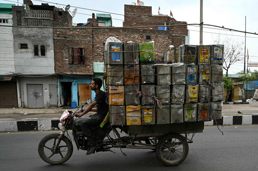 A worker transports empty oil tin canisters along a street in Amritsar, India, on 29 April 2024. (Narinder Nanu/AFP)