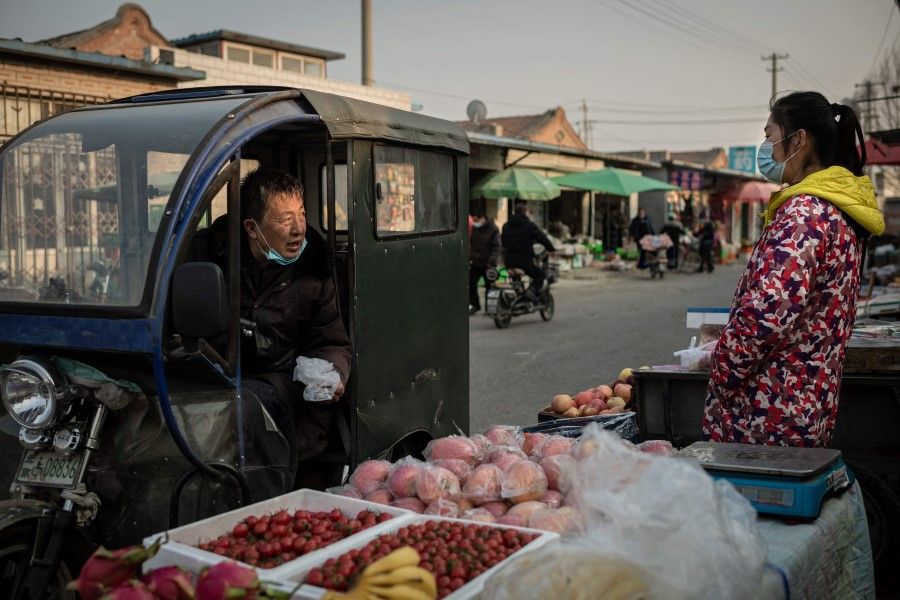 A driver (left) negotiates on the price of fruits with a vendor at a market on a street in Beijing on 25 February 2021. (Nicolas Asfouri/AFP)