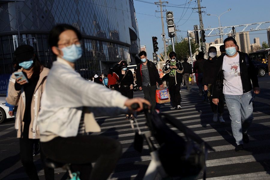 People wearing face masks walk across a street near a shopping mall in Beijing, China, 15 April 2022. (Tingshu Wang/Reuters)