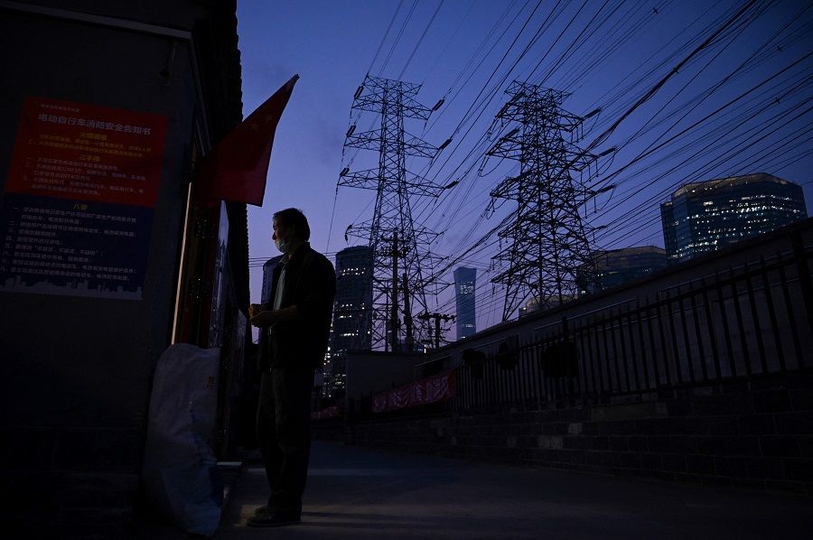 A man stands at a doorway below power lines in Beijing, China, on 28 September 2021. (Leo Ramirez/AFP)