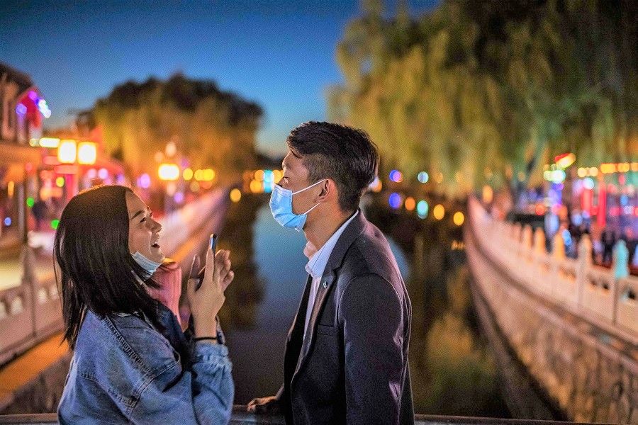 A couple wearing face masks share a laugh as they take pictures a bridge at the Hou Hai lake in Beijing on 16 October 2020. (Nicolas Asfouri/AFP)