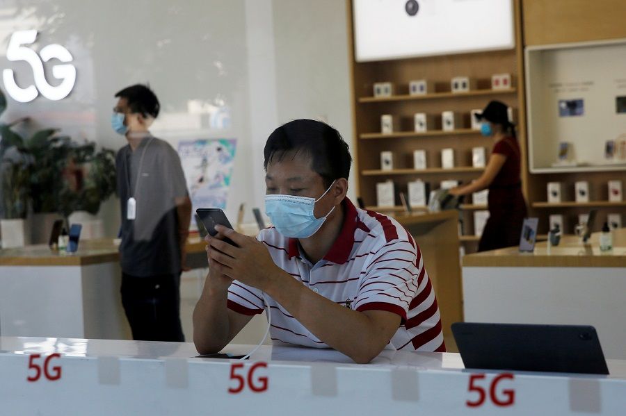A man wearing a face mask checks a mobile phone inside a Huawei store, at a shopping mall in Beijing, China, 14 July 2020. (Tingshu Wang/Reuters)
