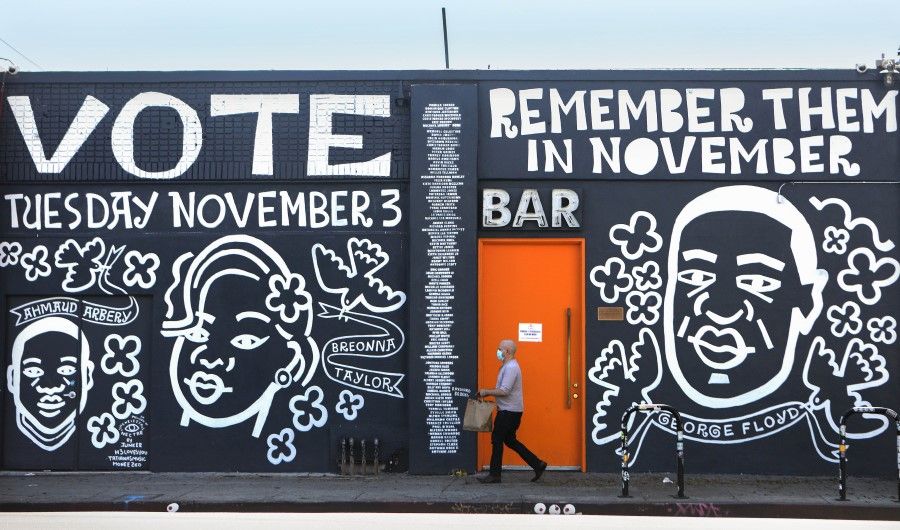 A man walks past a mural by artist Eric Junker which reads 'Vote- Remember Them In November' on 2 October 2020 in Los Angeles, California. The mural features images of deceased Black shooting victims George Floyd, Breonna Taylor and Ahmaud Arbery. (Mario Tama/AFP)