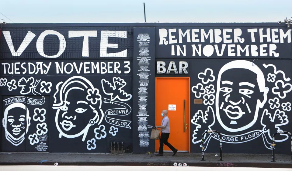 A man walks past a mural by artist Eric Junker which reads 'Vote- Remember Them In November' on 2 October 2020 in Los Angeles, California. The mural features images of deceased Black shooting victims George Floyd, Breonna Taylor and Ahmaud Arbery. (Mario Tama/AFP)