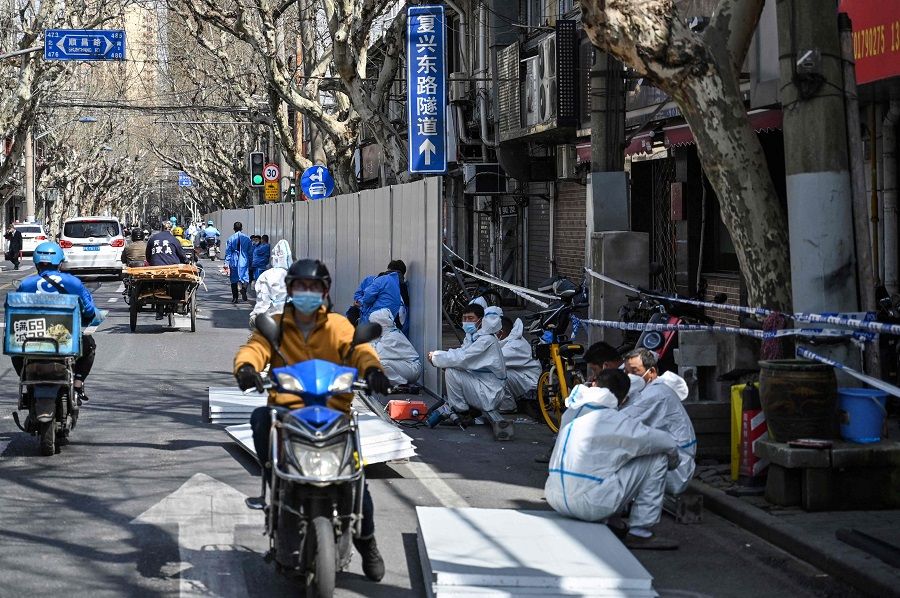 Officials (right in white) wearing protective gear work outside an area where barriers are being placed to close off streets around a locked down neighbourhood after the detection of new Covid-19 cases in Shanghai, China, on 15 March 2022. (Hector Retamal/AFP)