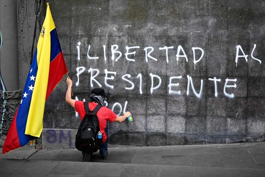 A demonstrator holding a Venezuelan flag paints a graffiti Freedom for president Nicolas (Maduro) during a march in Mexico City on 10 January 2026. (Alfredo Estrella/AFP)