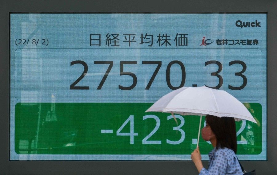 A woman walks past an electronic share price board showing the numbers on the Tokyo Stock Exchange in Tokyo on 2 August 2022. (Kazuhiro Nogi/AFP)