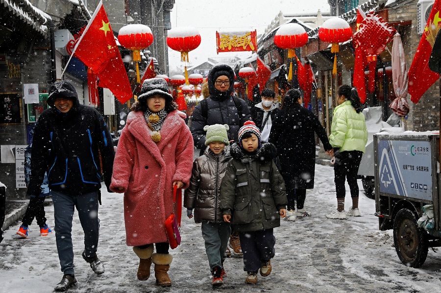 People walk at a hutong alley decorated with lanterns on a snowy day in Beijing, China, 13 February 2022. (Tingshu Wang/Reuters)