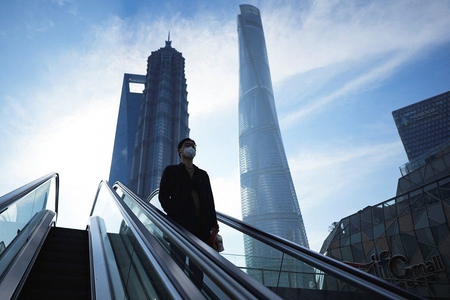 A man rides an escalator near office towers in the Lujiazui financial district in Shanghai, China, 28 February 2023. (Aly Song/Reuters)