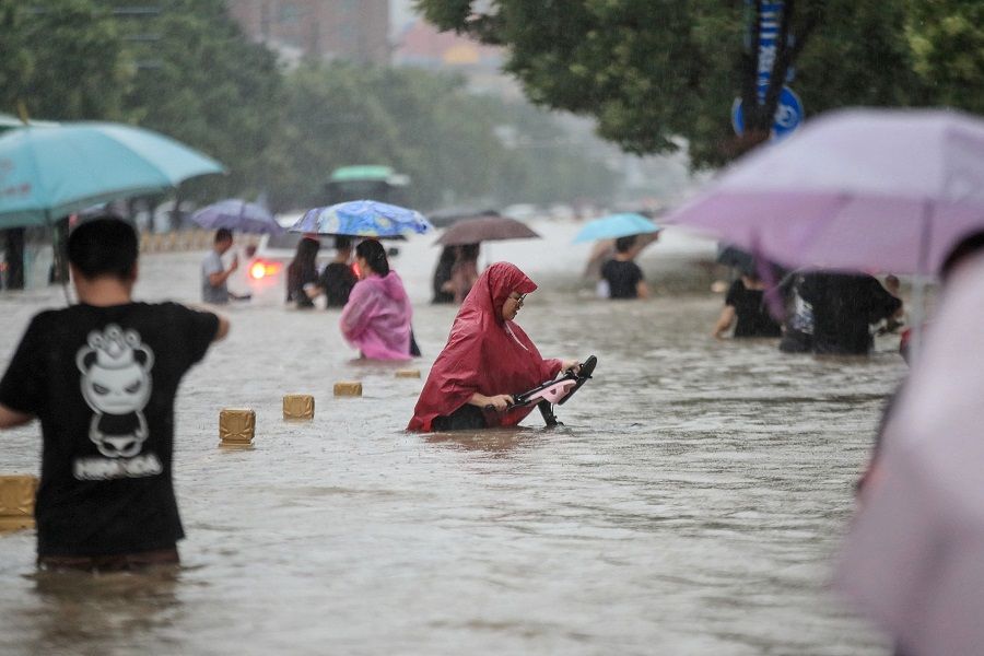 This photo taken on 20 July 2021 shows people wading through flood waters along a street following heavy rains in Zhengzhou, Henan province, China. (STR/AFP)
