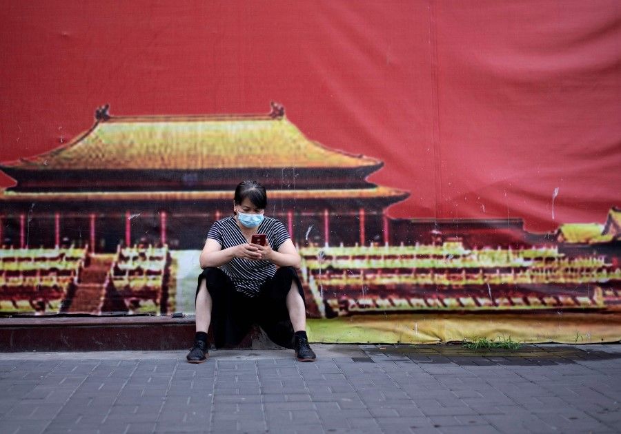 A woman wearing a face mask uses her mobile phone on a sidewalk in Beijing, 5 July 2020. (Noel Celis/AFP)