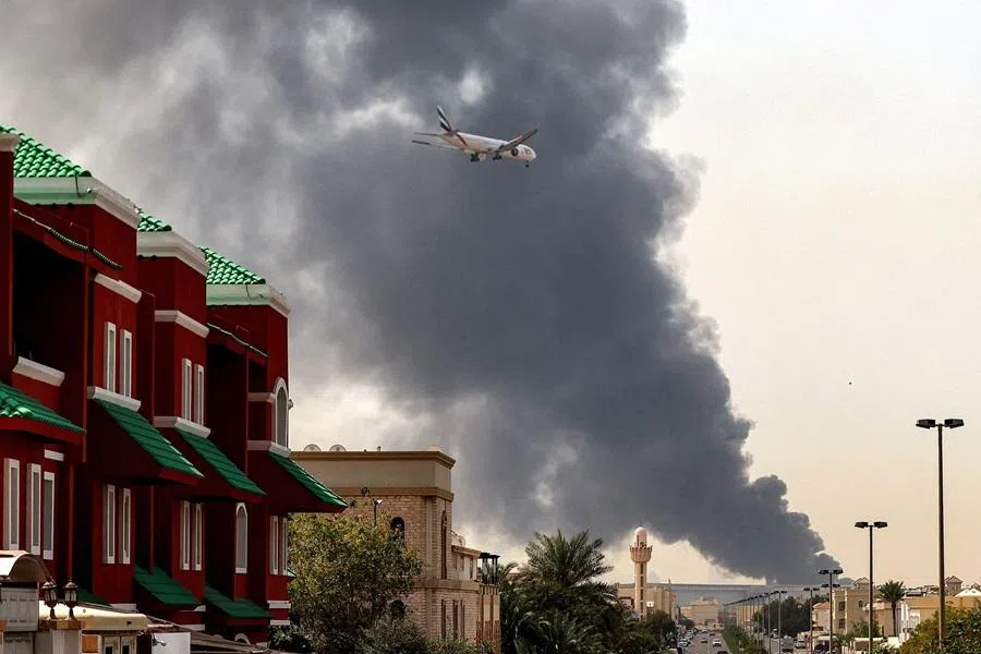 An Emirates aircraft prepares for landing as a smoke plume rises from an ongoing fire near Dubai International Airport in Dubai on 16 March 2026.